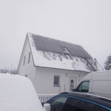 Montierte Solaranlage auf Hausdach im Schneetreiben.